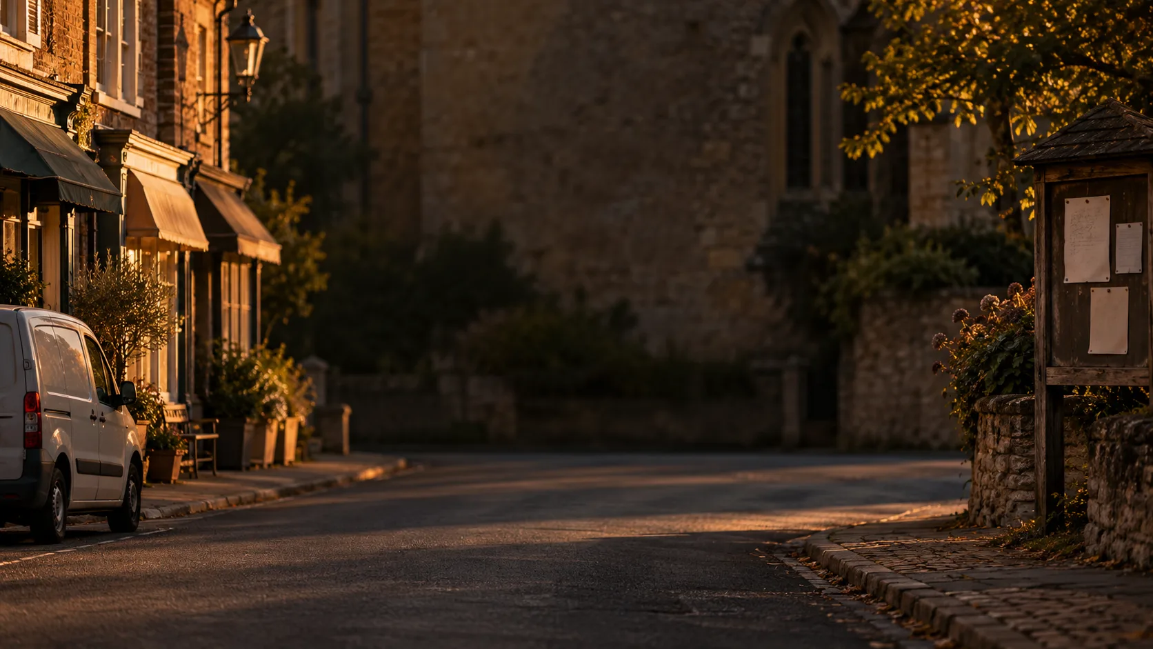 A quiet high street at dusk with shop awnings, a parked van and a noticeboard at the edge.