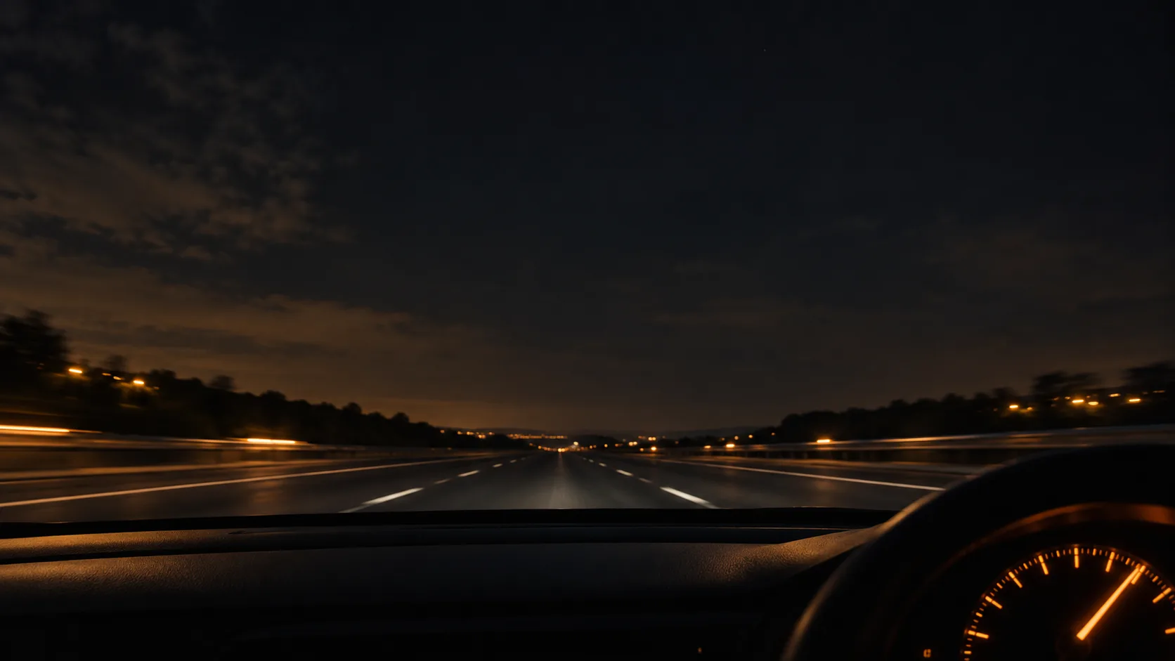 A car dashboard glowing at night with an empty motorway stretching ahead under a dark sky.