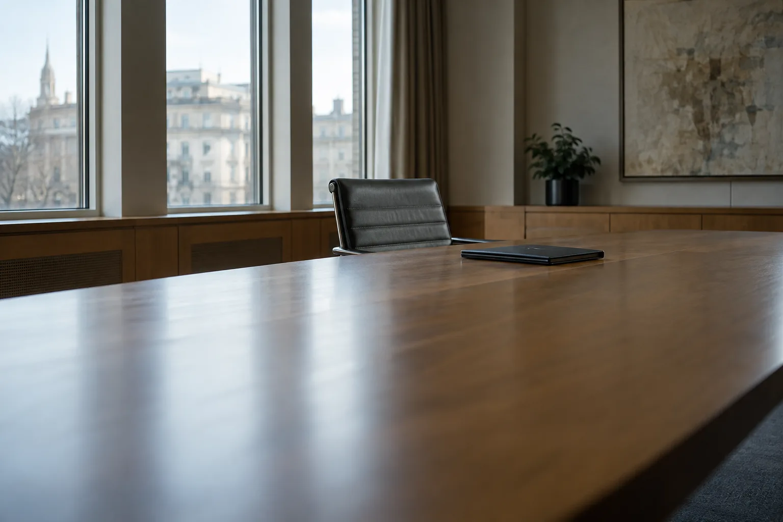 An empty chair at a bare boardroom table with a closed folder.